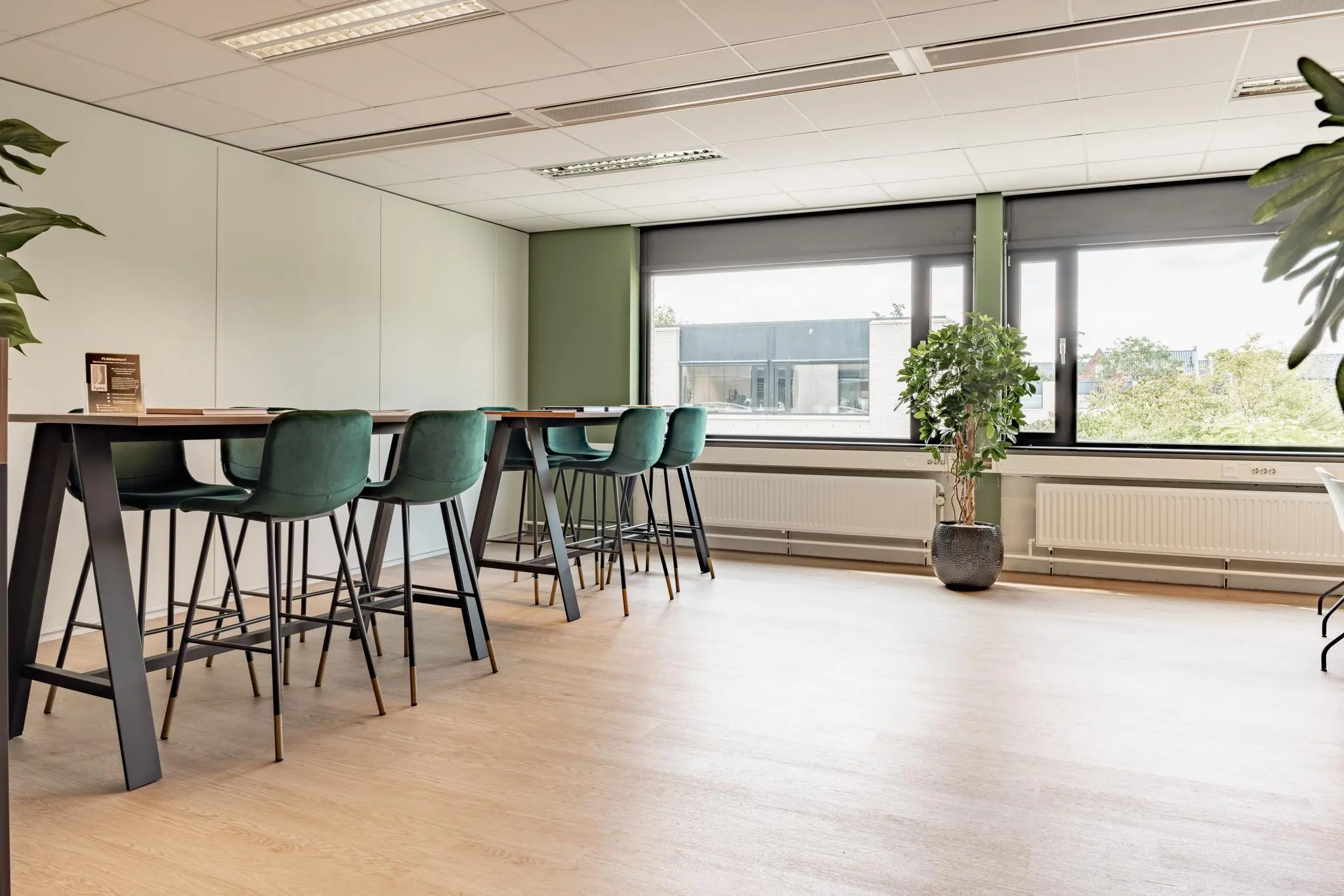 Moderne vergaderruimte met hoge tafels, groene barkrukken en grote ramen aan de Burgemeester Verderlaan.